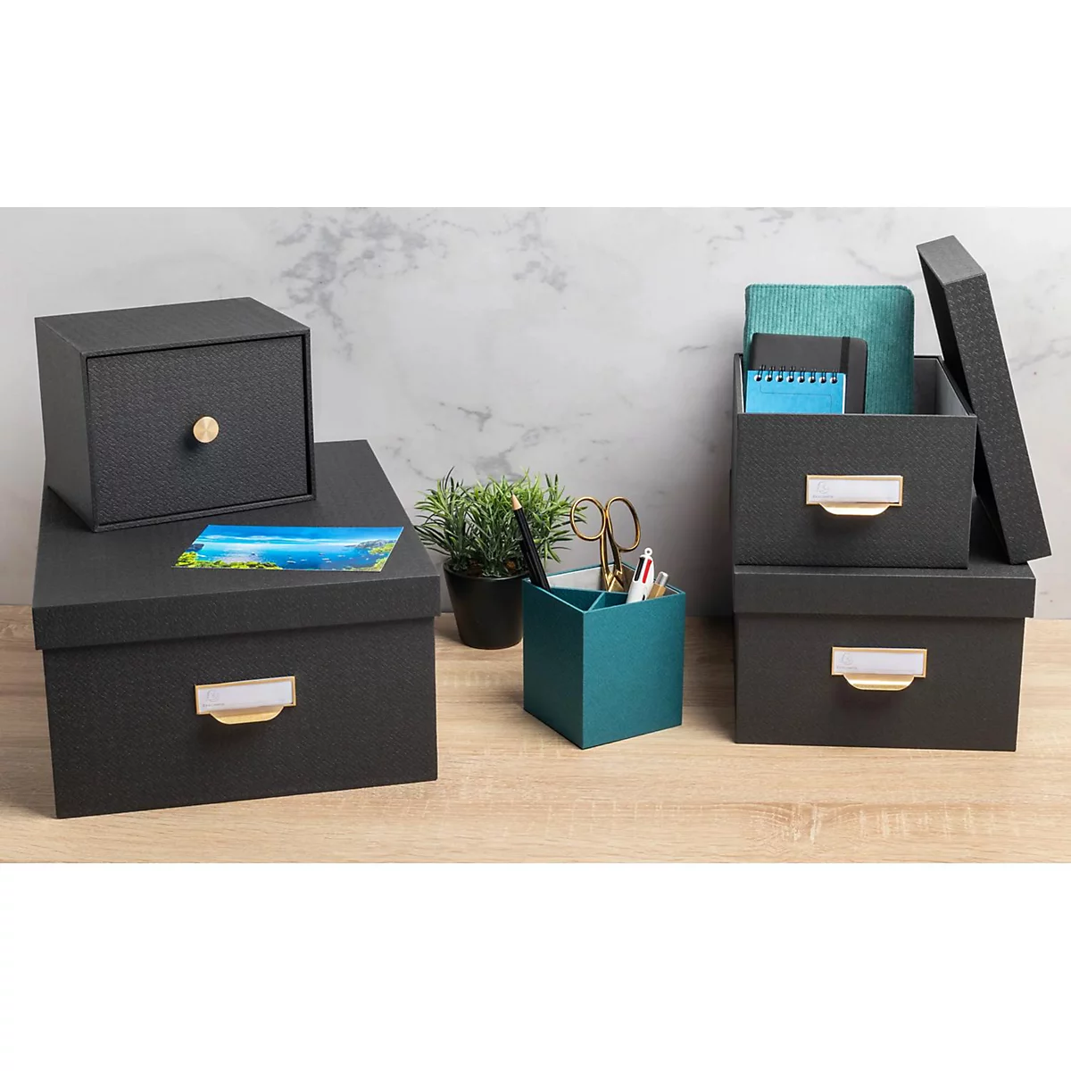 Dunkle Aufbewahrungsboxen mit Stifthalter, Notizbüchern und Schere, auf Holzplatte.