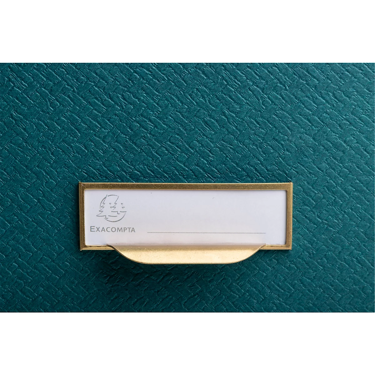 Gros plan sur une surface vert foncé texturée avec une étiquette rectangulaire en papier clair et un cadre en laiton. "EXACOMPTA" est écrit en dessous.