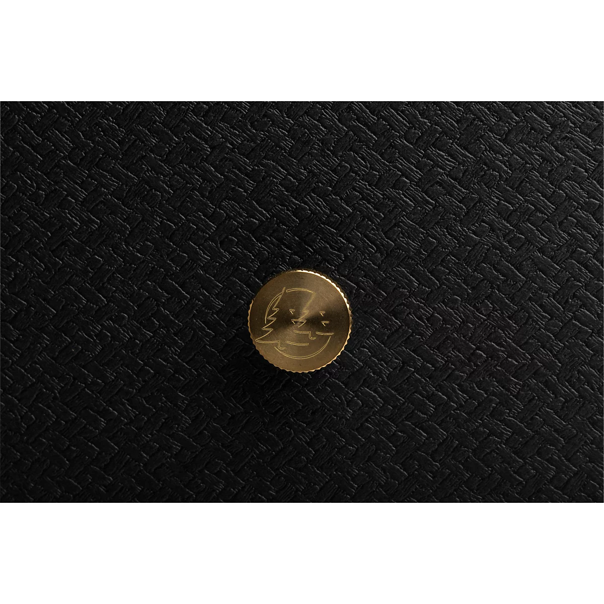 Detailopname: Gouden knop met logo op zwarte, getextureerde achtergrond.