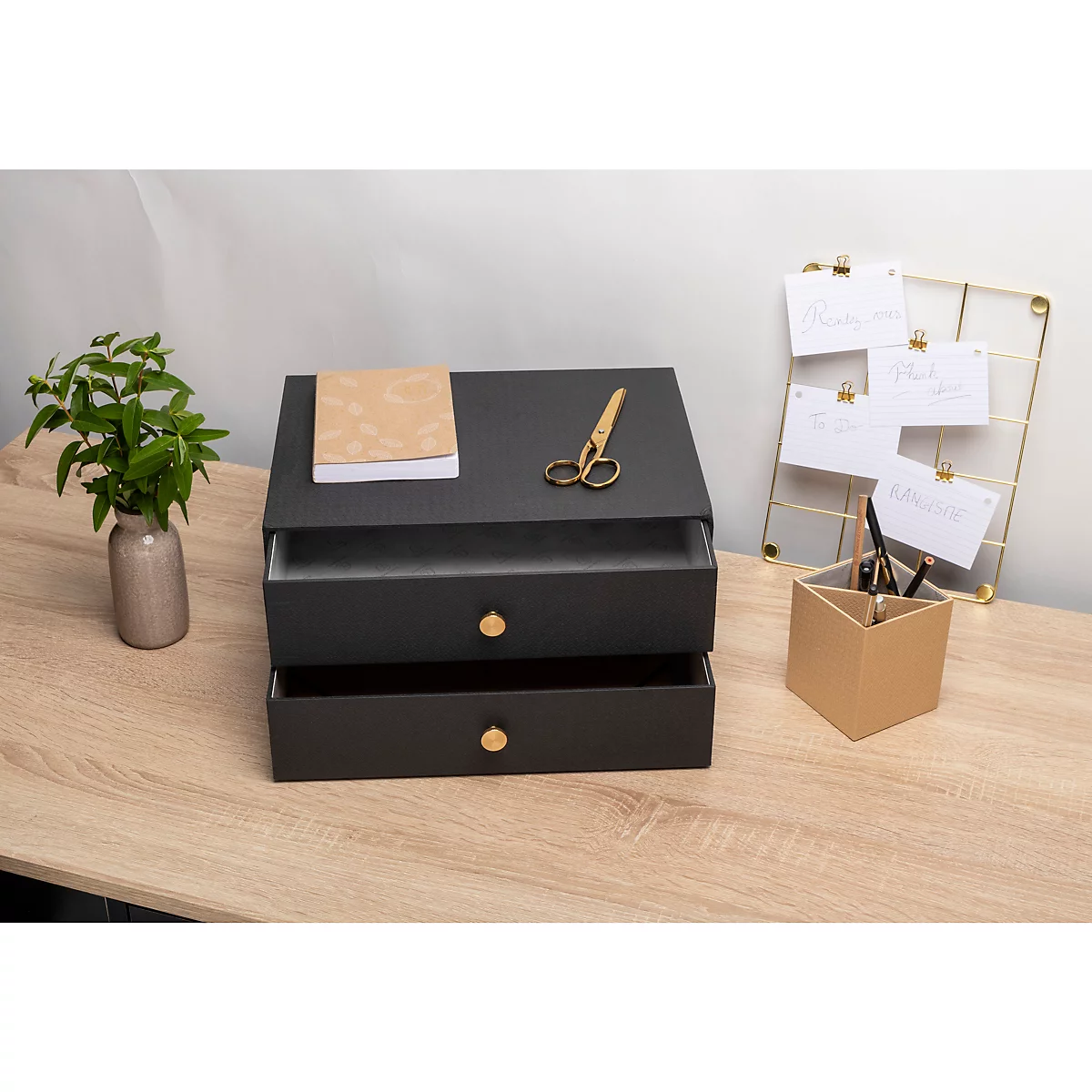 Dunkle Schubladenbox mit Notizblock, Schere und Pflanzen auf einem Holztisch.