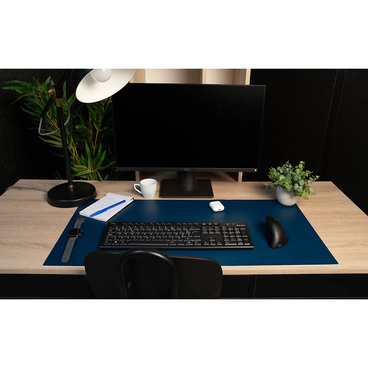 Schreibtisch mit Monitor, Tastatur und Accessoires. Blaue Tischunterlage, eine Uhr und eine Kaffeetasse.