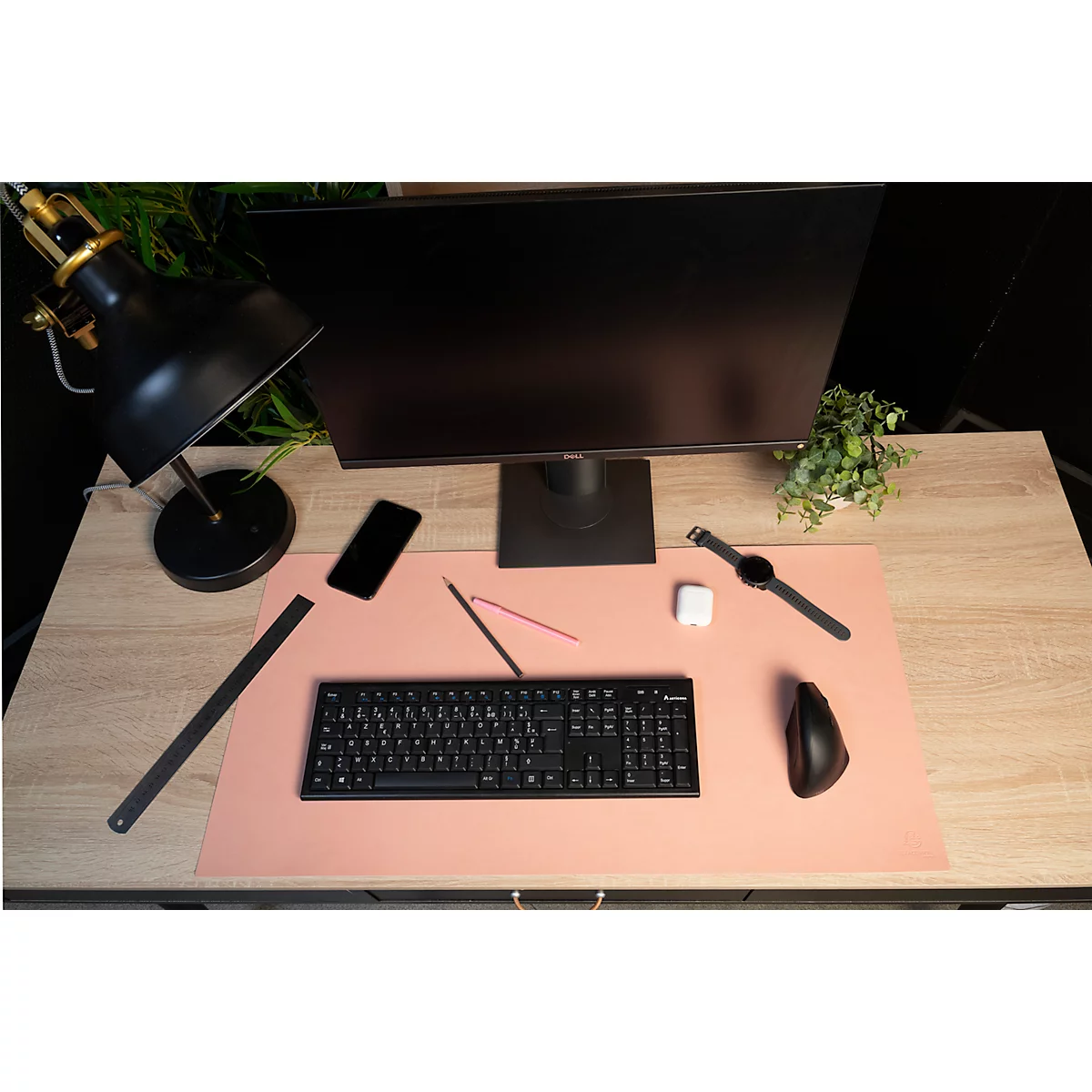 Schreibtisch mit Monitor, Tastatur, Uhr, Handy, Lampe und Maus. Rosa Matte, helles Holz. Alles ist ordentlich angeordnet.
