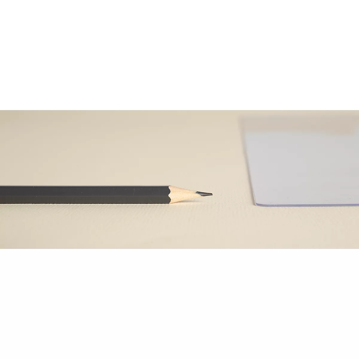 Ein schwarzer Bleistiftspitze und ein transparentes Lineal liegen auf hellem Papier. Der Bleistift zeigt auf die Spitze.