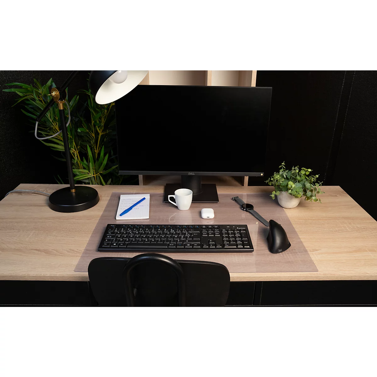 Ein Schreibtisch mit Computer, Tastatur, Maus, Becher, Notizblock, Stift, Kopfhörer und Lampe.