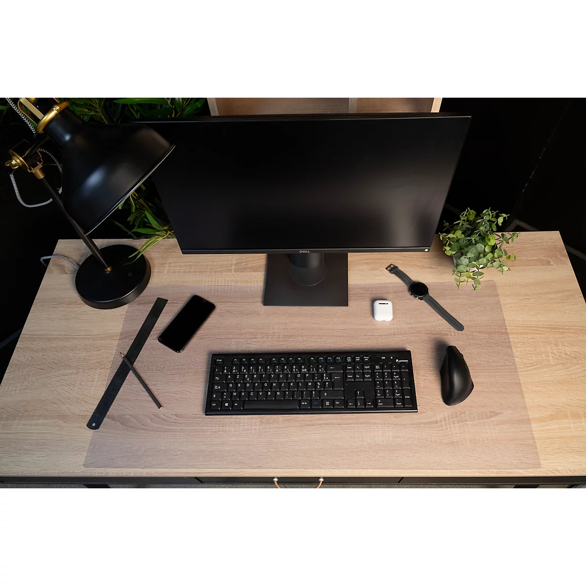 Draufsicht auf einen Schreibtisch mit Monitor, Tastatur, Maus, Uhr, Smartphone und Lampe.