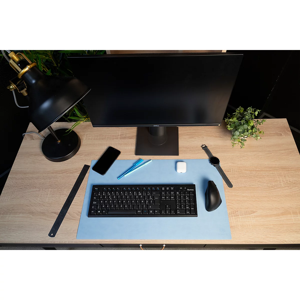 Schreibtisch mit Monitor, Tastatur, Maus, Uhr, Stiften, Handy und Lampe. Holzoptik, blauer Untergrund.