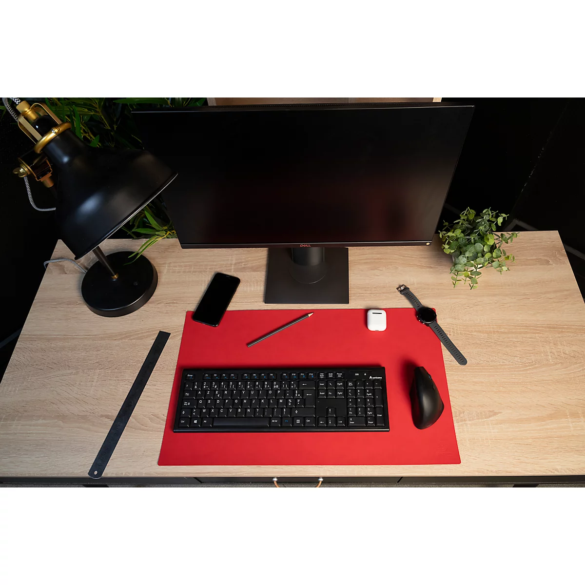 Schreibtisch mit Monitor, Tastatur, Maus, Uhr, Handy, Stift, Lampe, Lineal, und Pflanze.