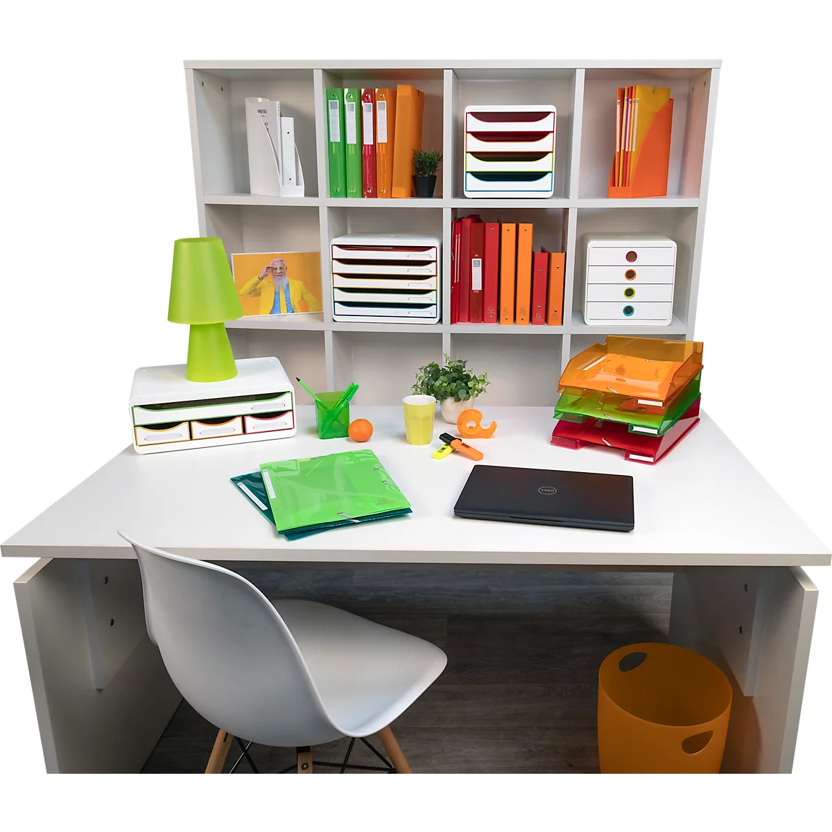 Ein weißer Schreibtisch mit einer Regalkombination, gefüllt mit Ordnern und Büromaterialien. Auf dem Tisch ein Laptop, bunte Ablagen und eine Lampe.