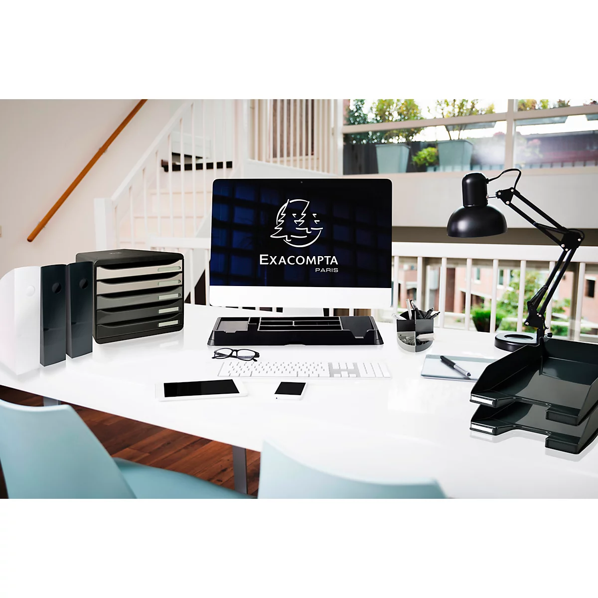 Schreibtisch mit Monitor, Schubladen, Lampe und Smartphone. Auf dem Monitor ist das Logo von Exacompta Paris.