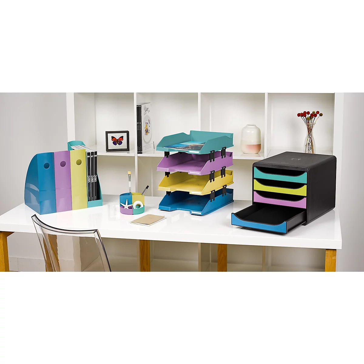 Büro-Organizer mit Schubladen, Stifthalter, farbige Ablagekörbe und Ordner. Schreibtisch vor einem Regal mit Dekoration.