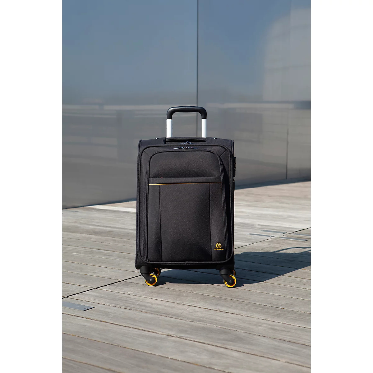 Valise noire avec poignée rétractable sur un sol en bois. Roues jaunes.