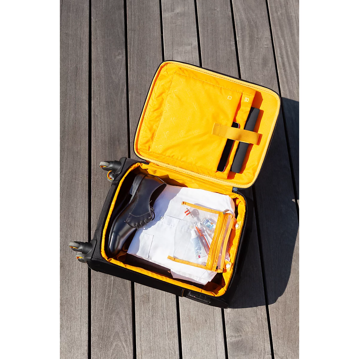 Geöffnete, gelb gefütterte, schwarze Handgepäck-Trolley. Darin ein Schuh, Beutel, Utensilien.