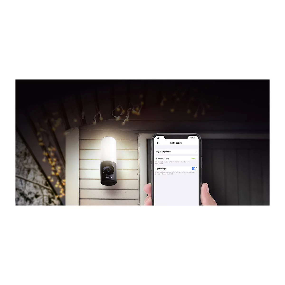 Kamera mit Licht und Smartphone, das die Einstellungen zeigt. Die Kamera ist an der Hauswand angebracht, das Licht ist eingeschaltet.