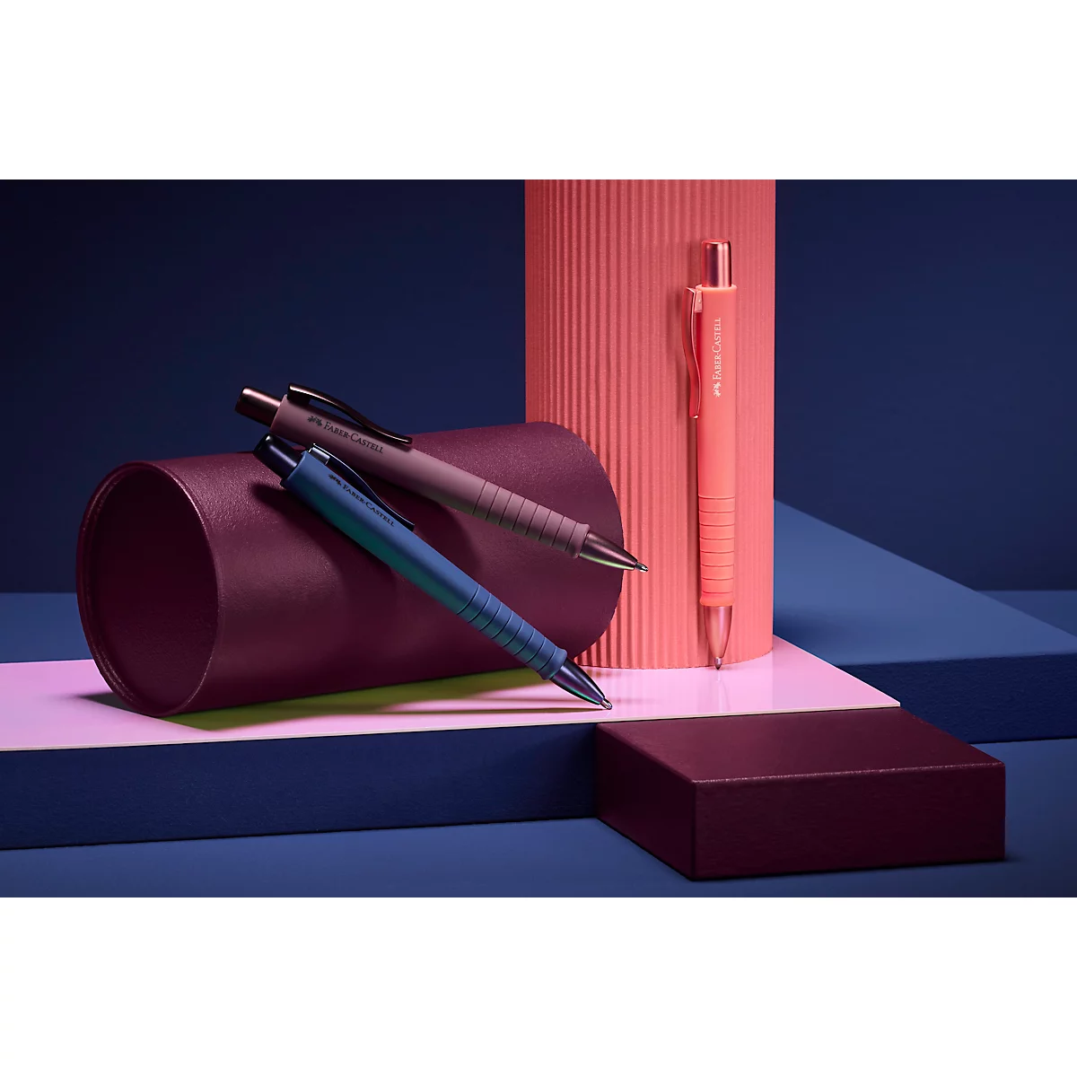 Trois stylos à bille de différentes couleurs : bleu, marron et orange. Éléments décoratifs, tels que des objets cylindriques et cubiques.