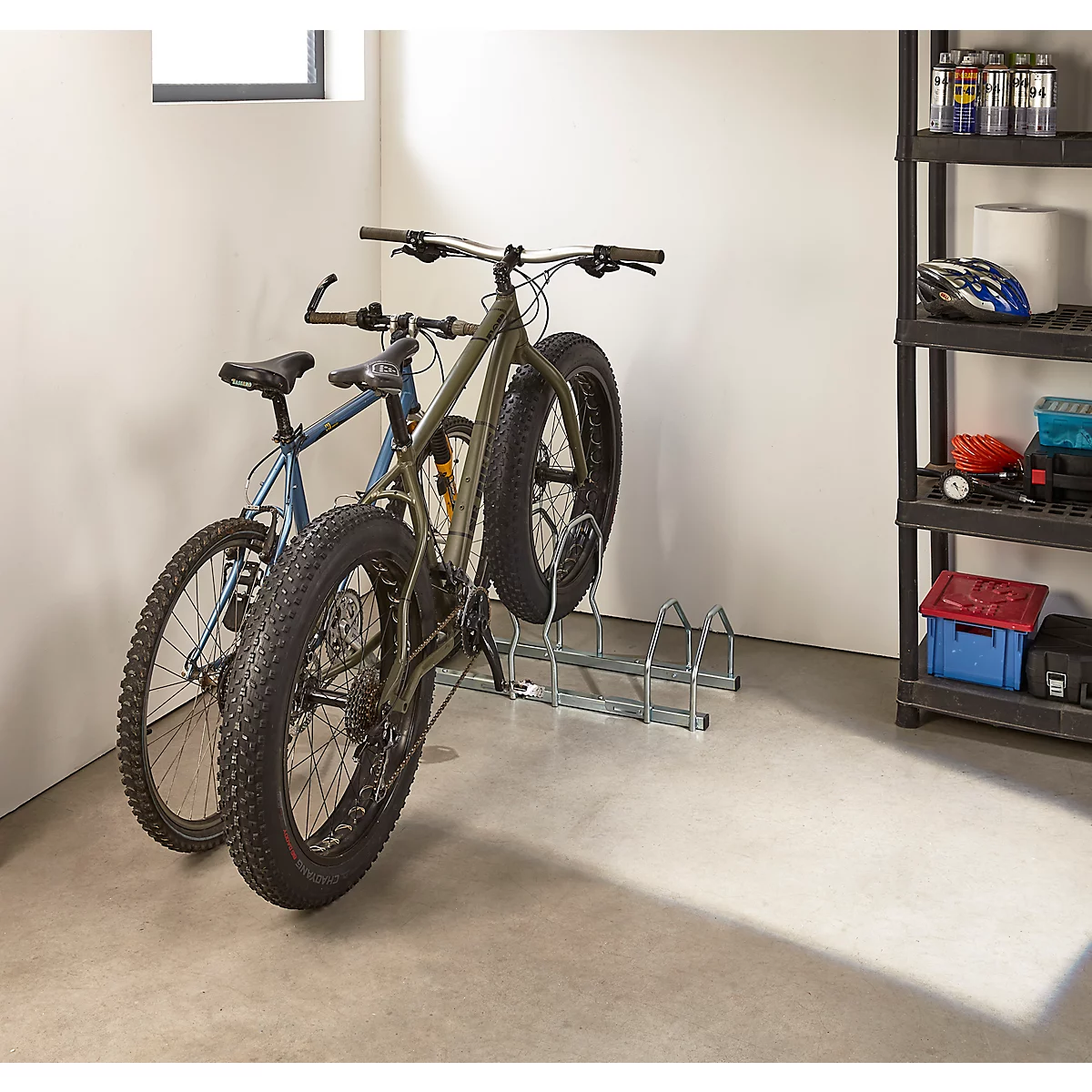 Zwei Fahrräder stehen in einer Garage in einem Fahrradständer. Eines ist ein Fatbike.