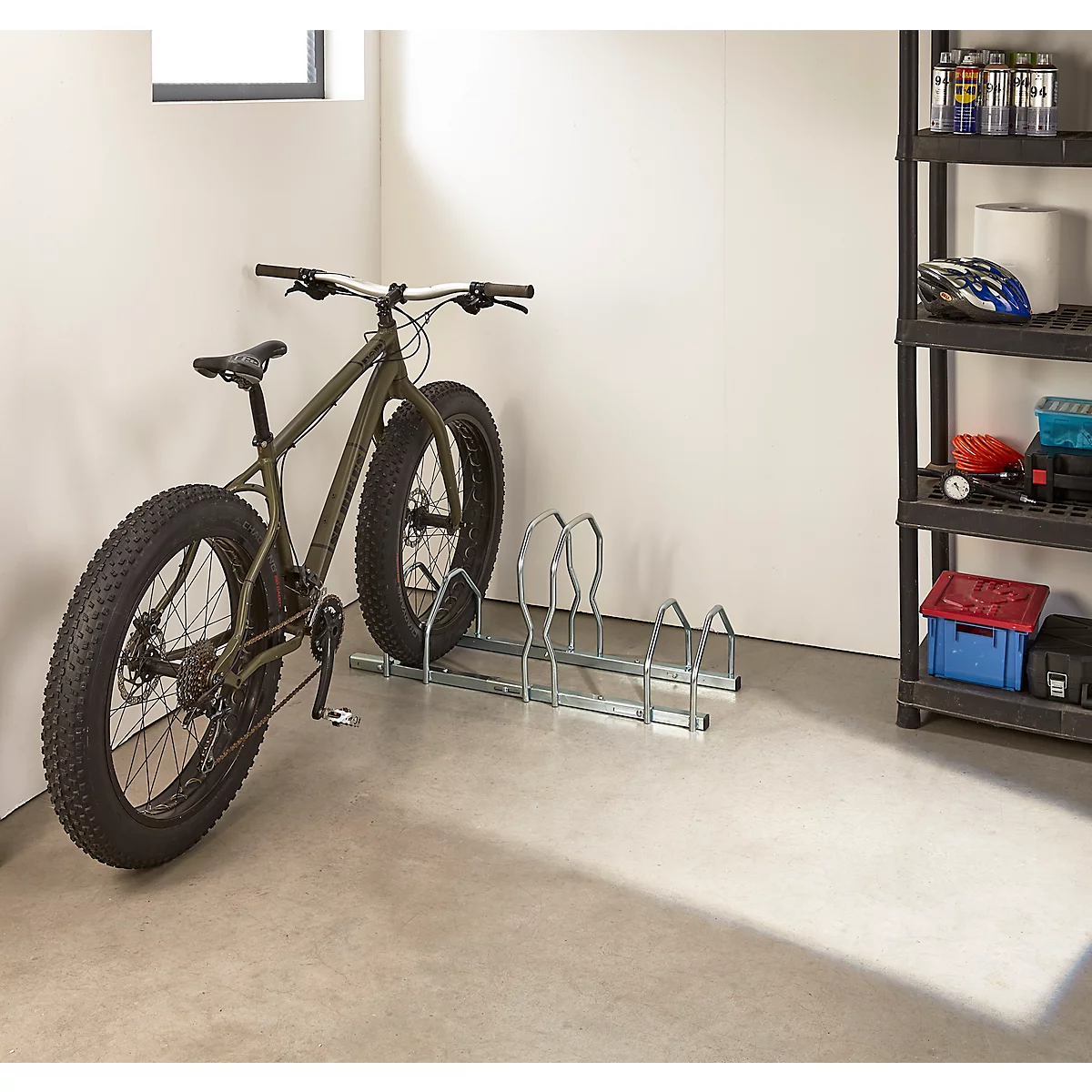 Fahrrad steht in einer Garage vor einem Fahrradständer. Aufbewahrung von Zubehör auf einem Regal.
