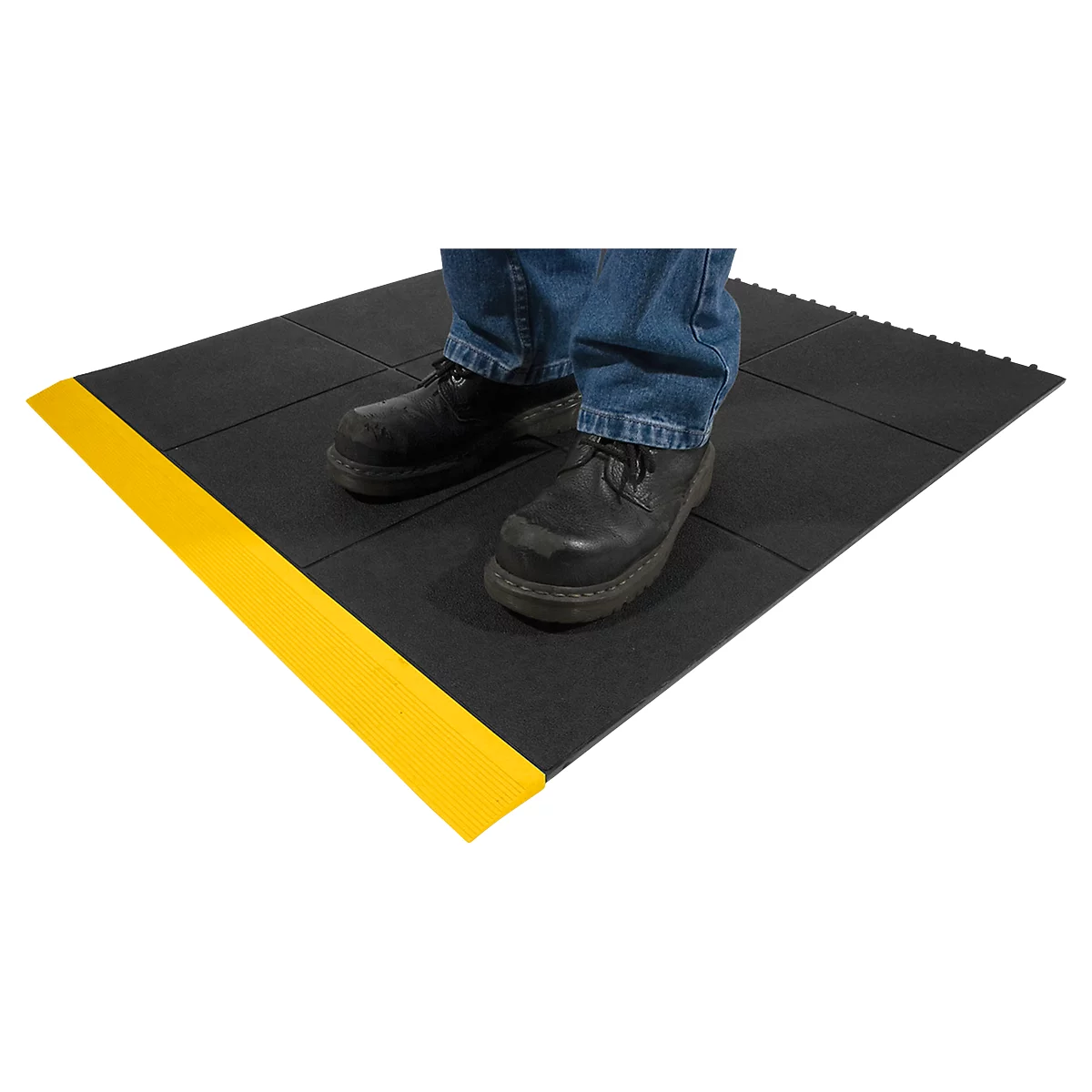A person stands on a black anti-slip mat with a yellow edge. Feet are in black shoes and jeans.