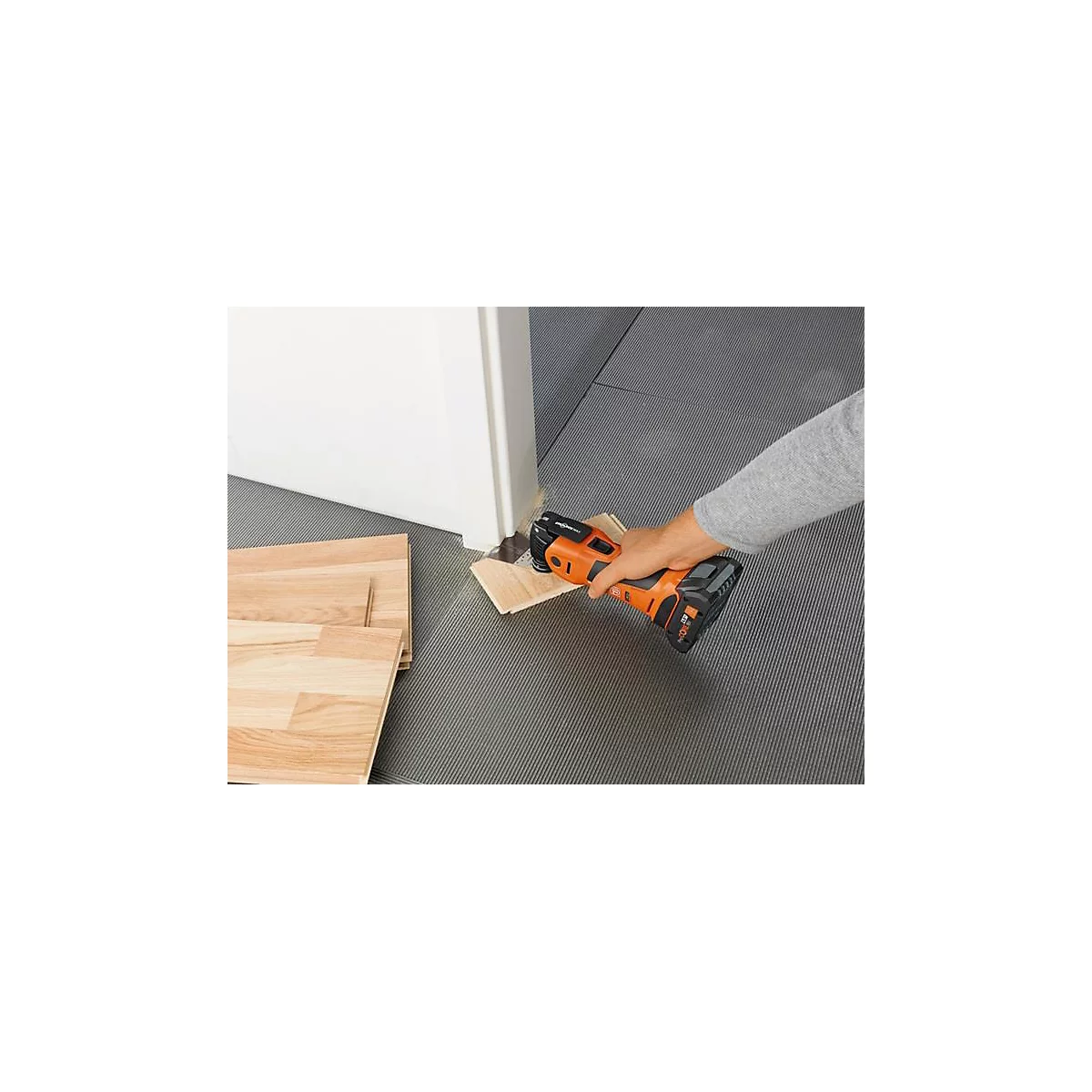Une personne coupe un morceau de bois sous une porte avec un outil oscillant. D'autres morceaux de bois sont sur le sol.