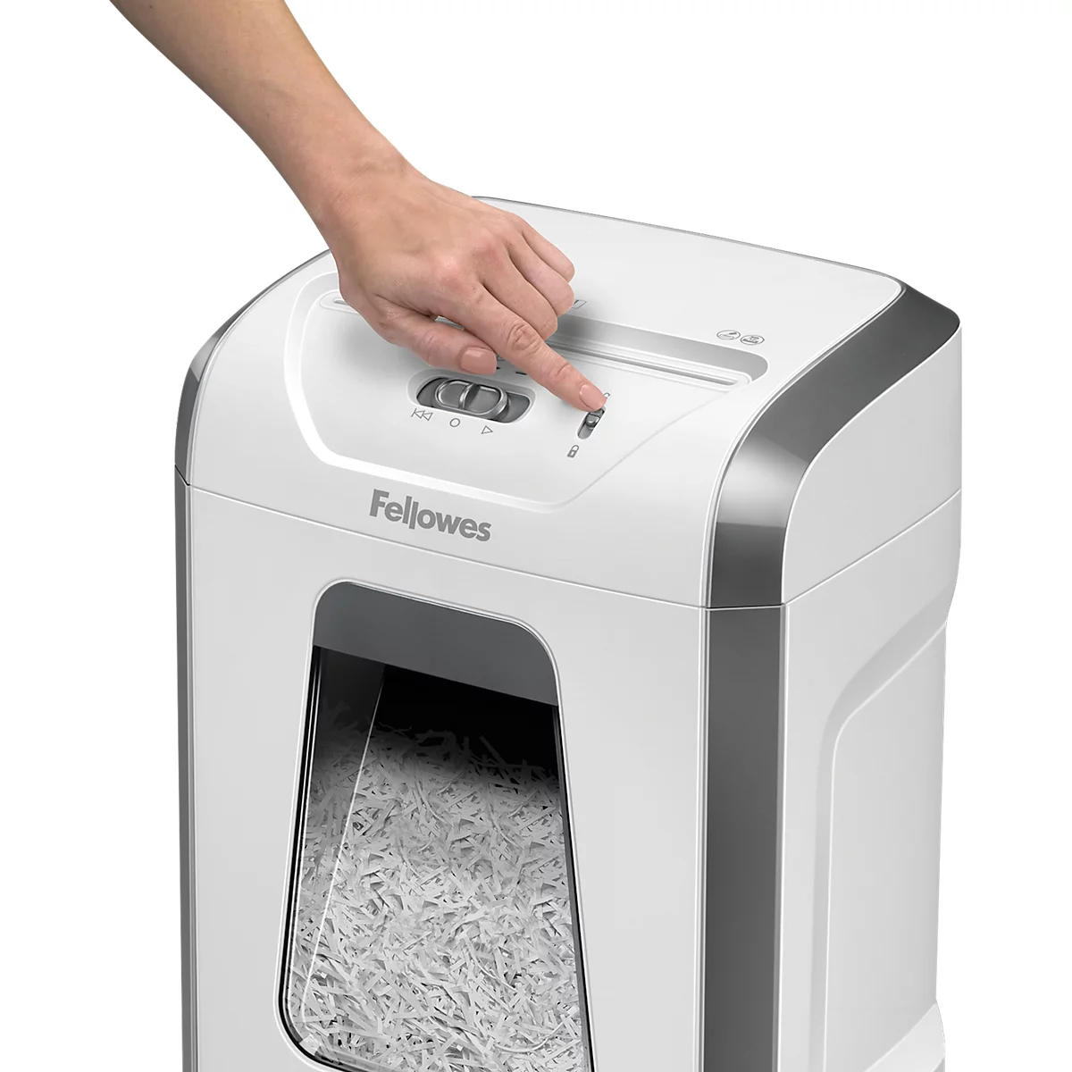 A hand presses a button on a white Fellowes paper shredder.