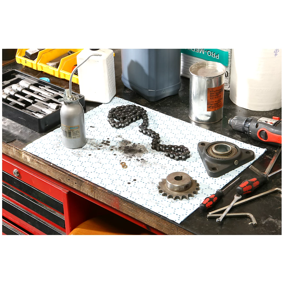 Une chaîne, un pignon, des outils et une burette d'huile reposent sur une table.