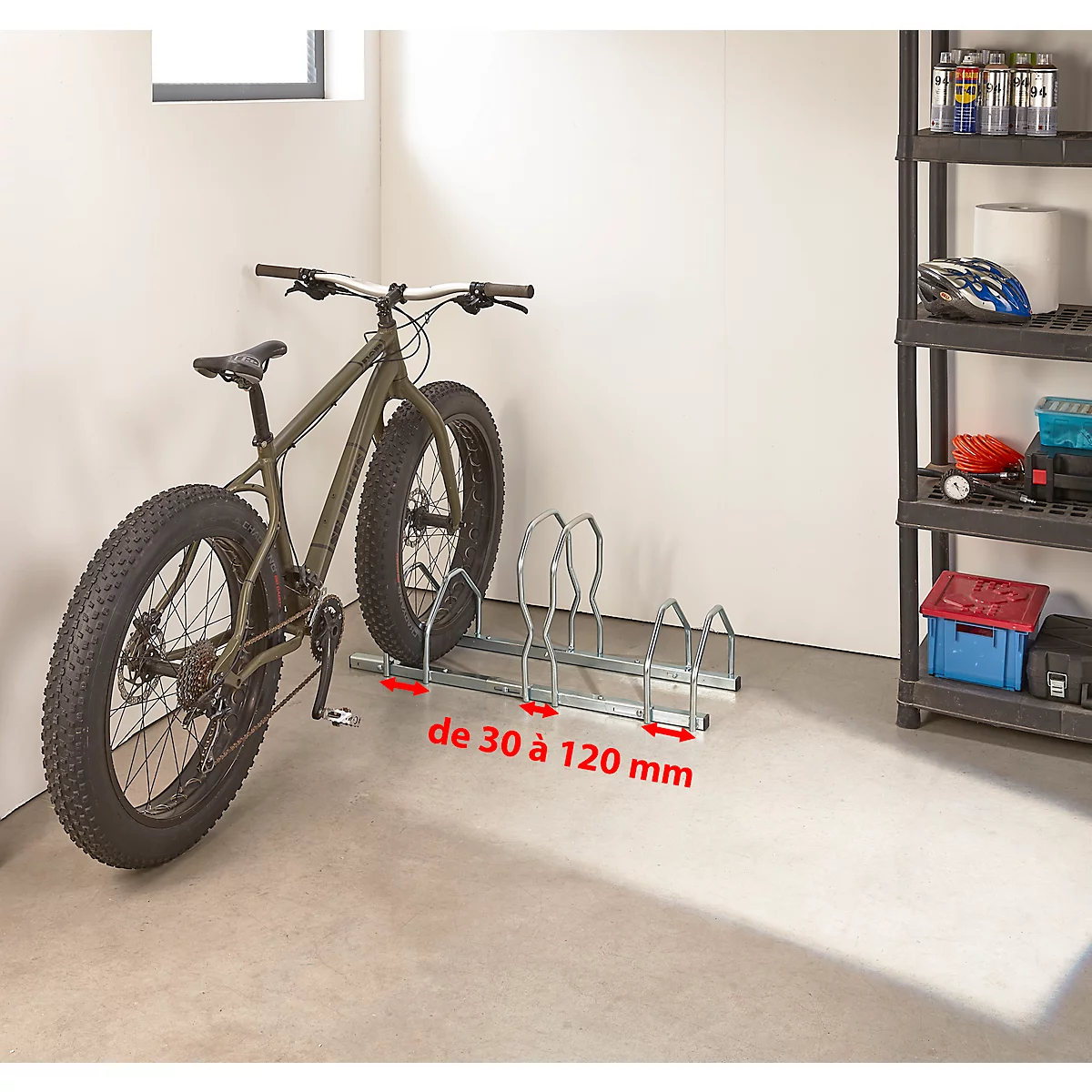Een groene fatbike staat in een fietsenrek met de tekst "de 30 à 120 mm". Op een plank ernaast liggen spullen.