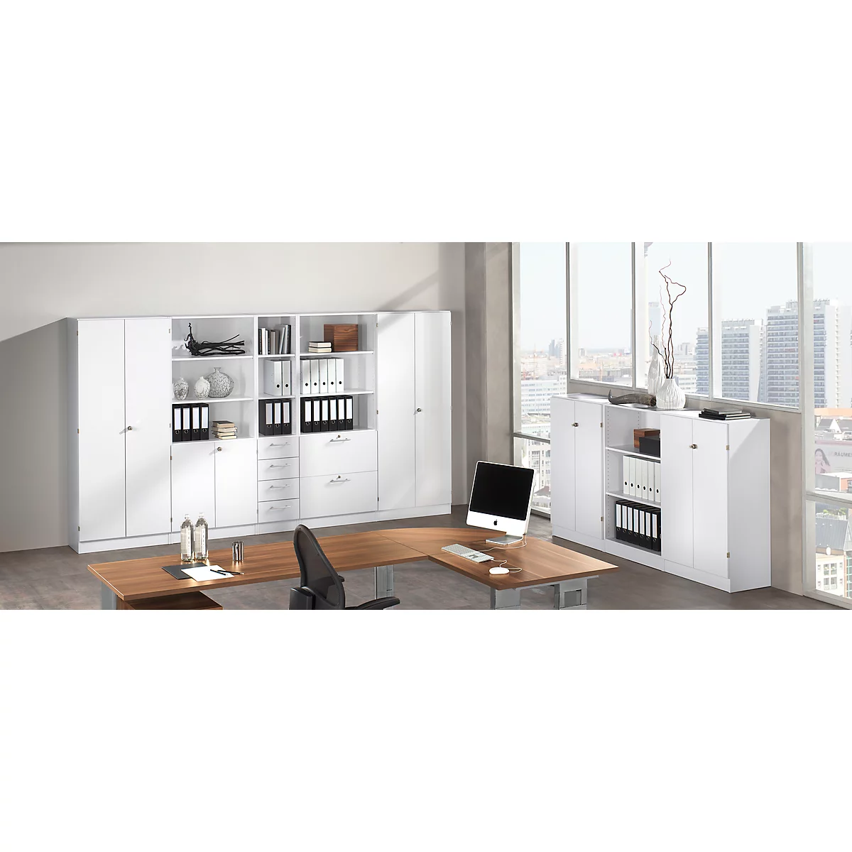 An office with white cabinet, wooden desk and window with view of a city.