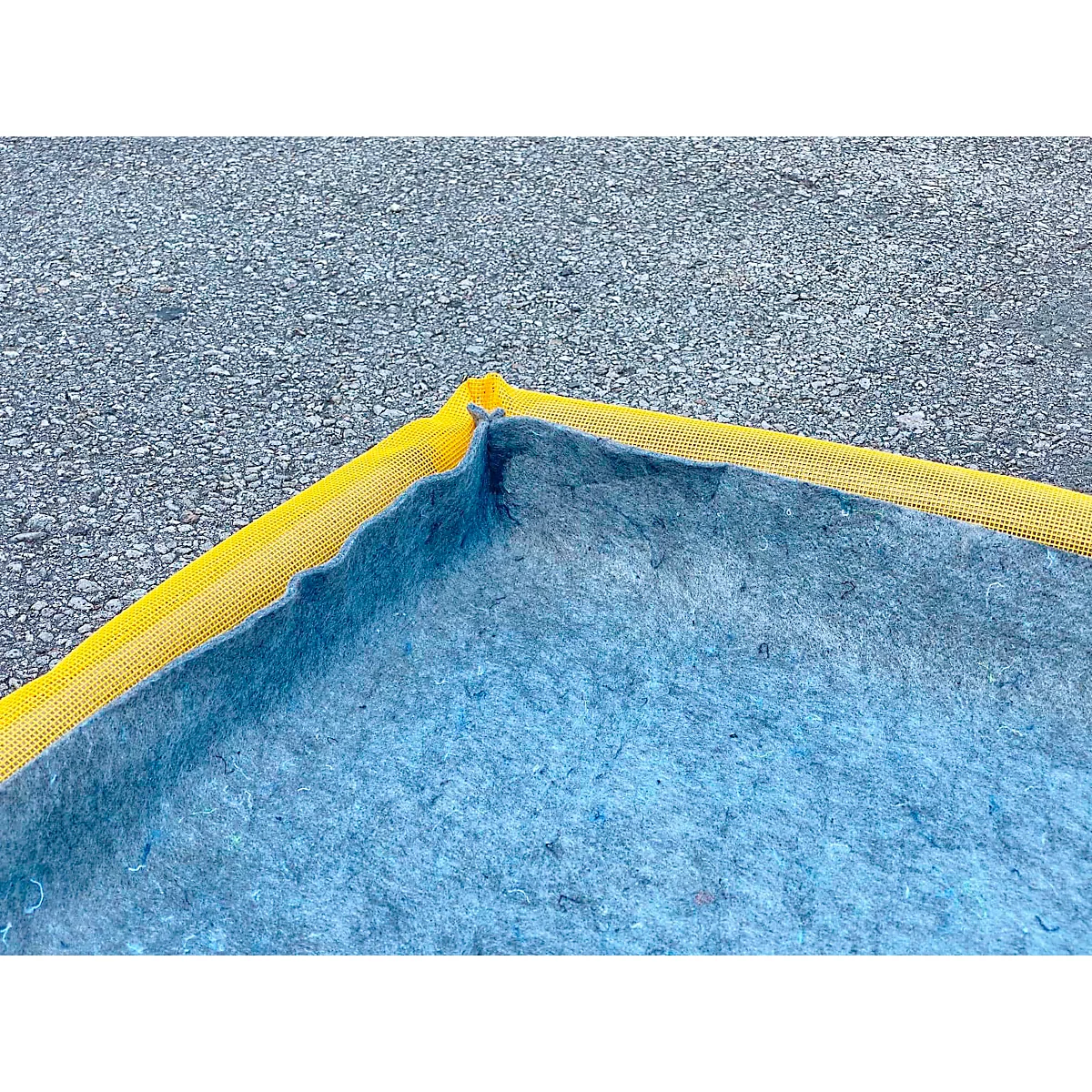 Hoek van een blauw zeil met een gele rand, op een grijze ondergrond.