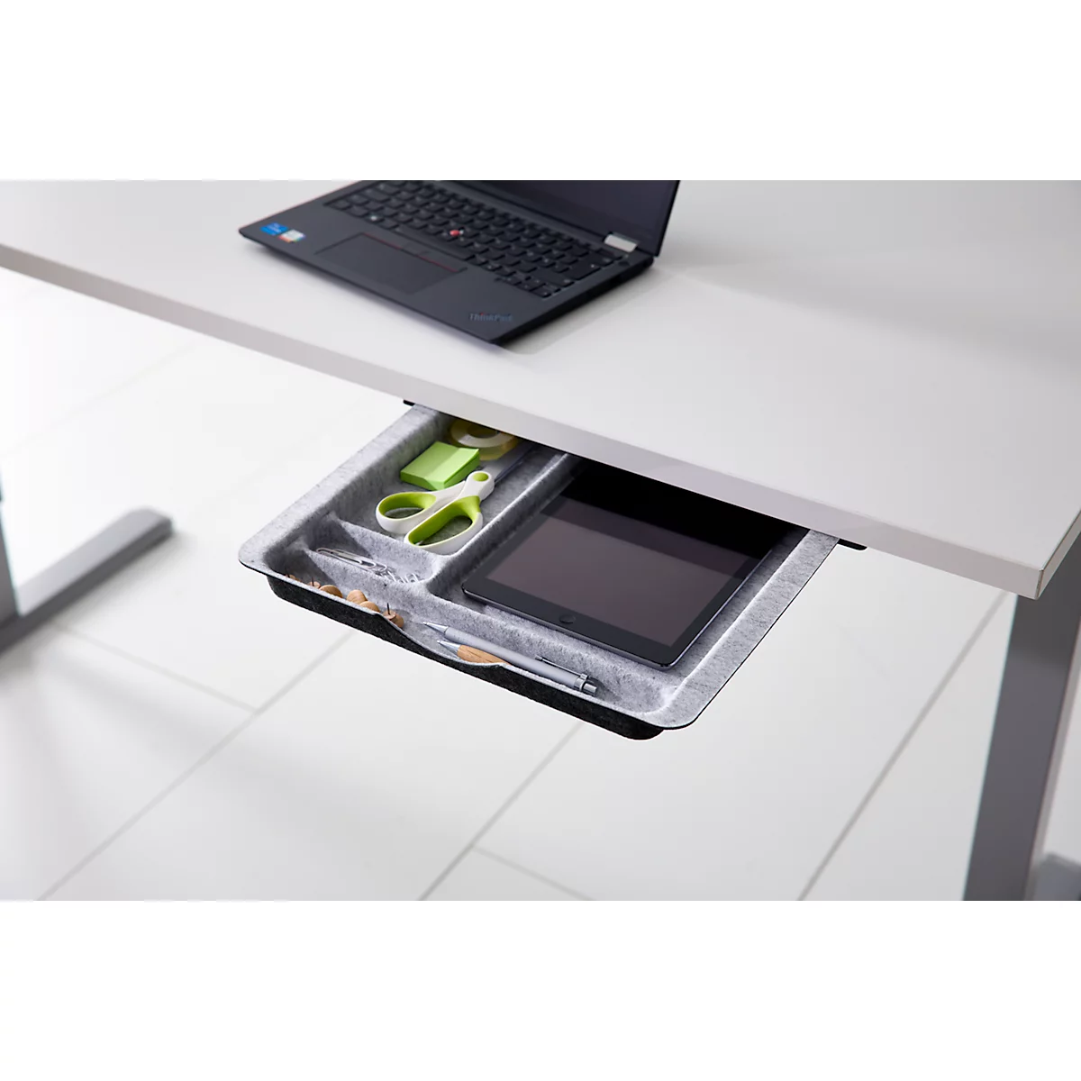 Eine geöffnete Schreibtischschublade mit Stiften, einer Schere, Haftnotizen und einem Tablet.