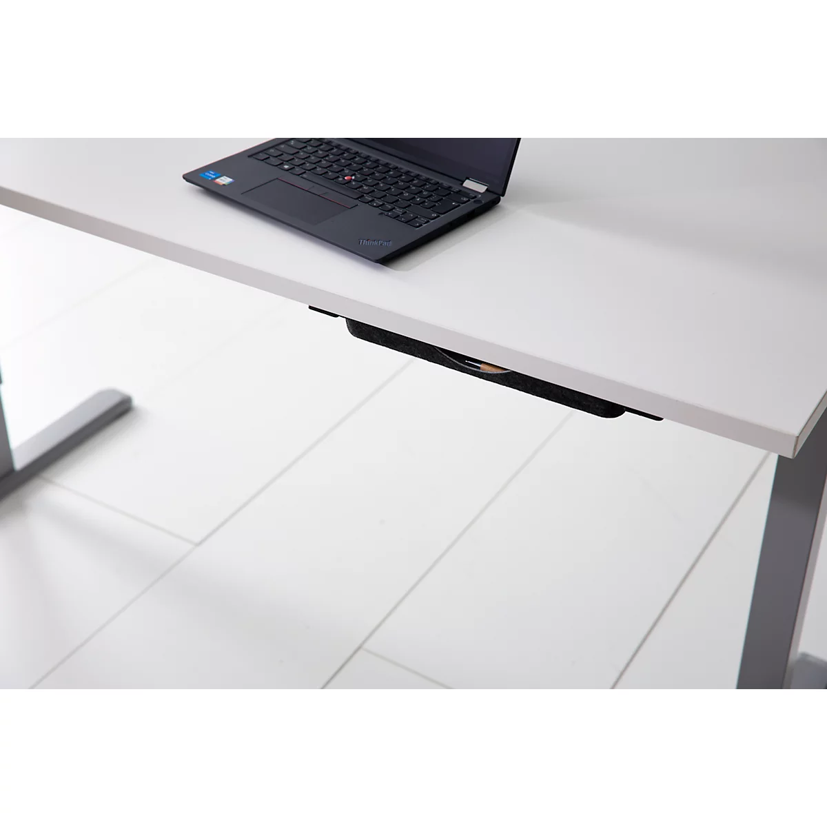 Ein heller Schreibtisch mit einem schwarzen Laptop und einer montierten, schwarzen Schublade unter der Tischplatte.