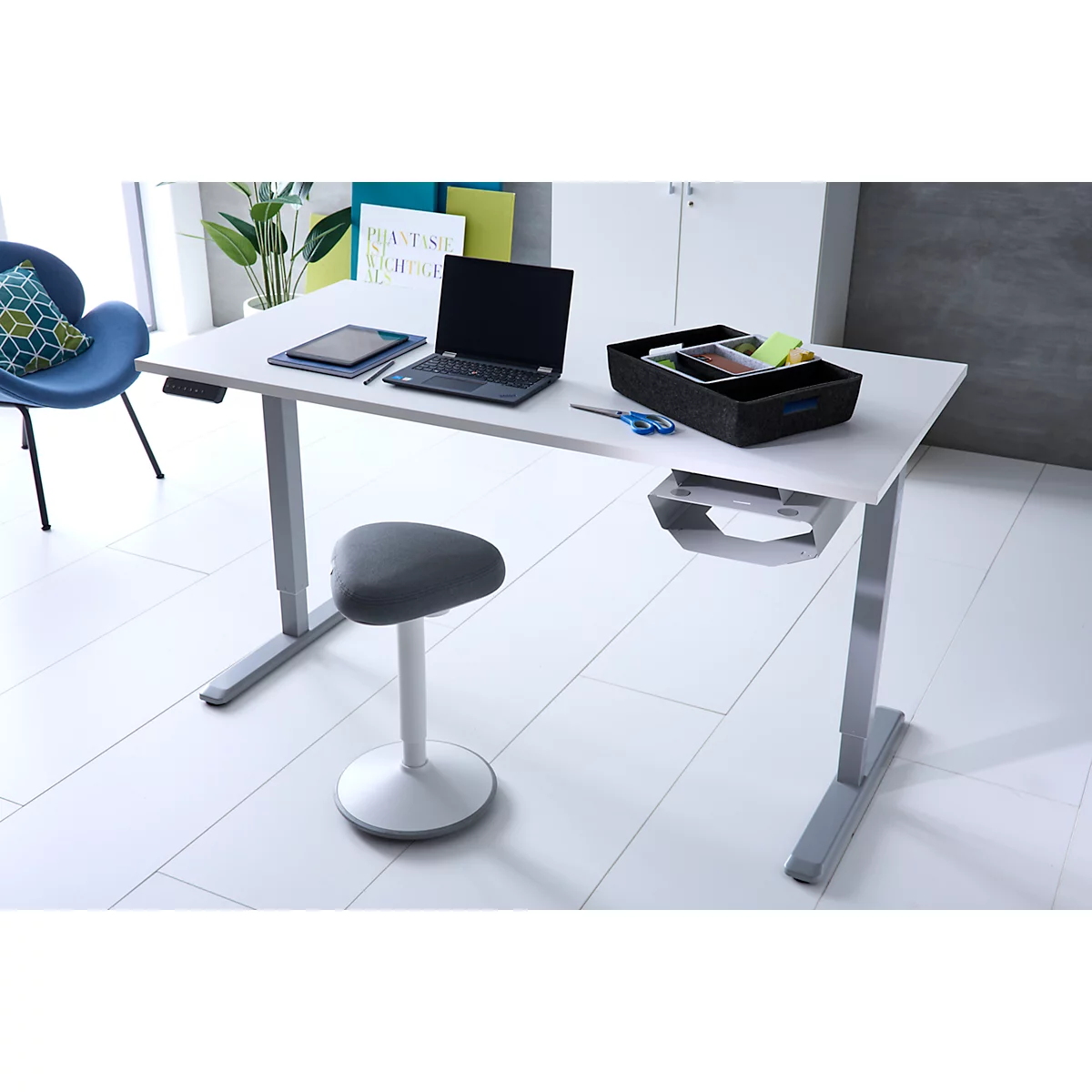 Ein moderner, höhenverstellbarer Schreibtisch mit einem Laptop, Tablet und Organizer. Ein ergonomischer Hocker steht davor.