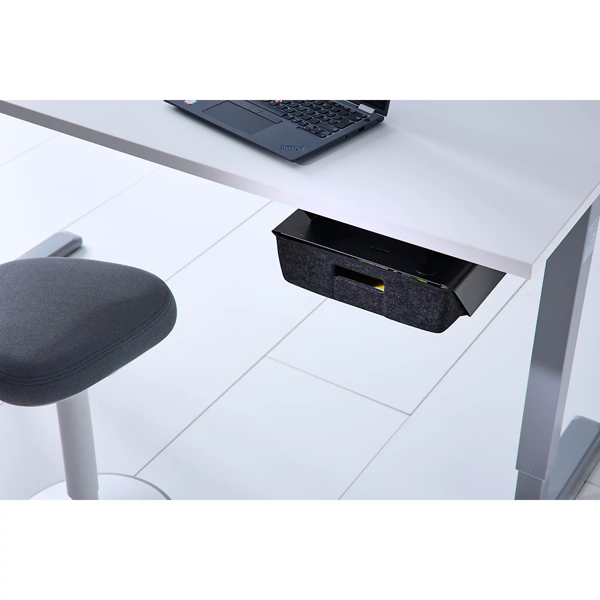 Eine unter einem weißen Schreibtisch montierte, graue Filzschublade mit einem Laptop auf dem Tisch.