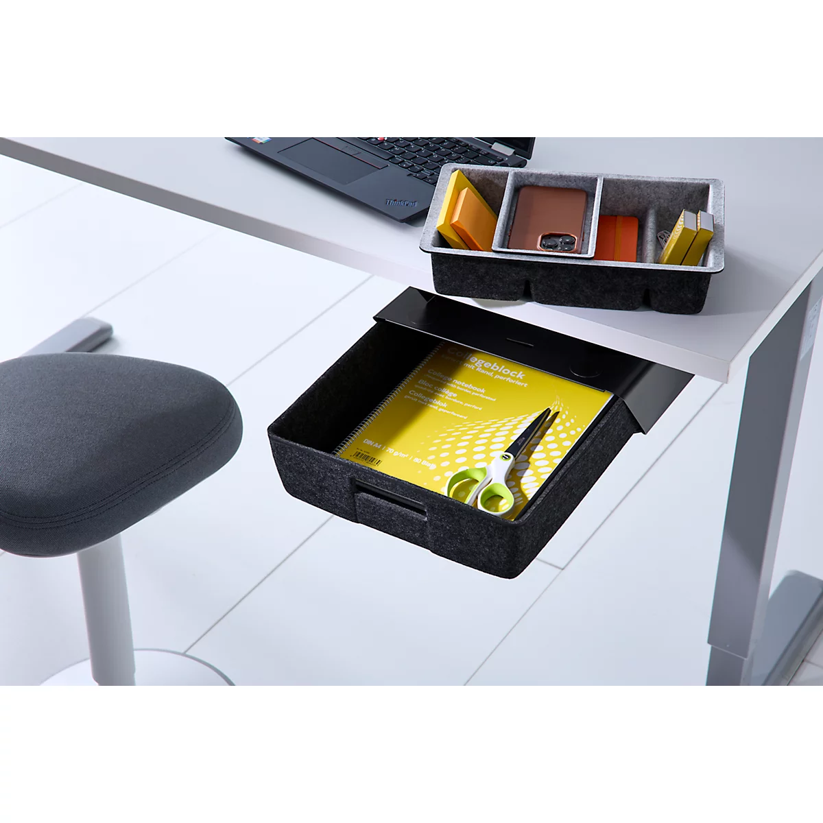 Ausziehbare Schublade unter einem Schreibtisch mit Notizblock und Schere, daneben ein Organizer auf dem Tisch.