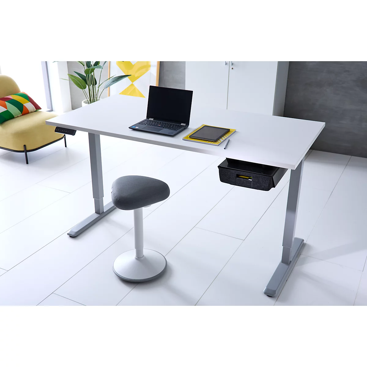Höhenverstellbarer Schreibtisch mit weißer Platte, Laptop und grauem Hocker in modernem Büro.