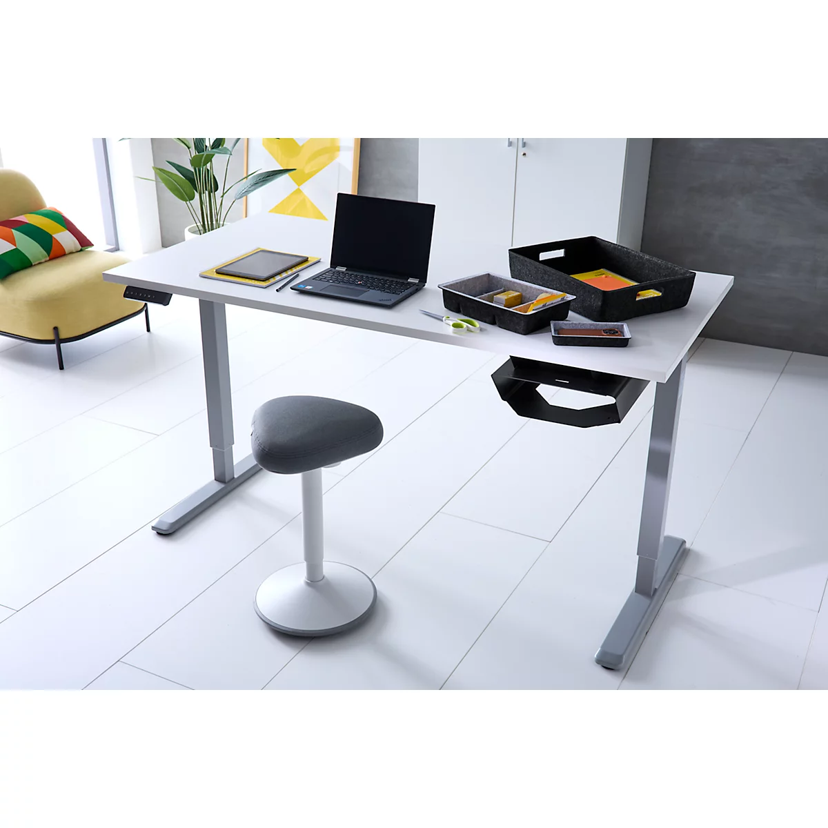 Ein moderner, höhenverstellbarer Schreibtisch mit Laptop und Zubehör in einem hellen, aufgeräumten Büro.