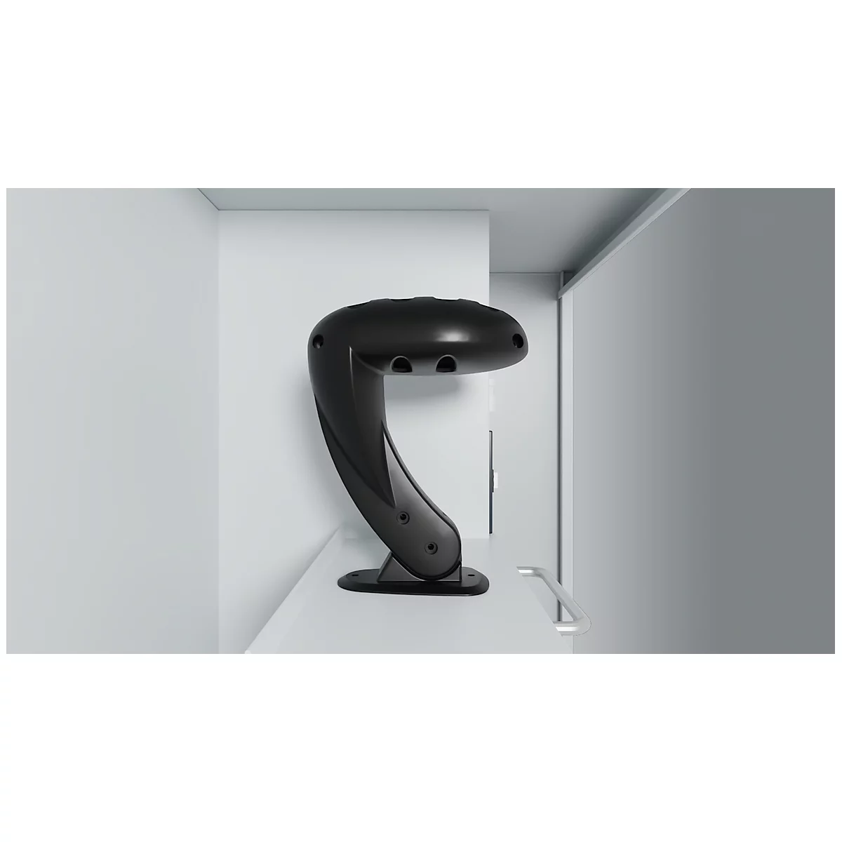 Black, curved lamp with three light openings, placed on a white surface, against a gray background.