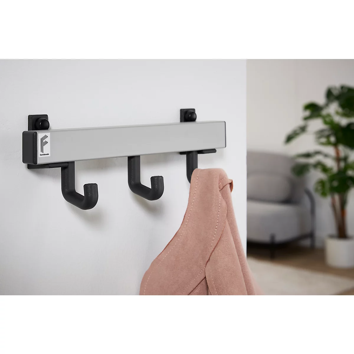 Un porte-manteau avec trois crochets noirs, avec une veste rose. Le porte-manteau est accroché au mur.