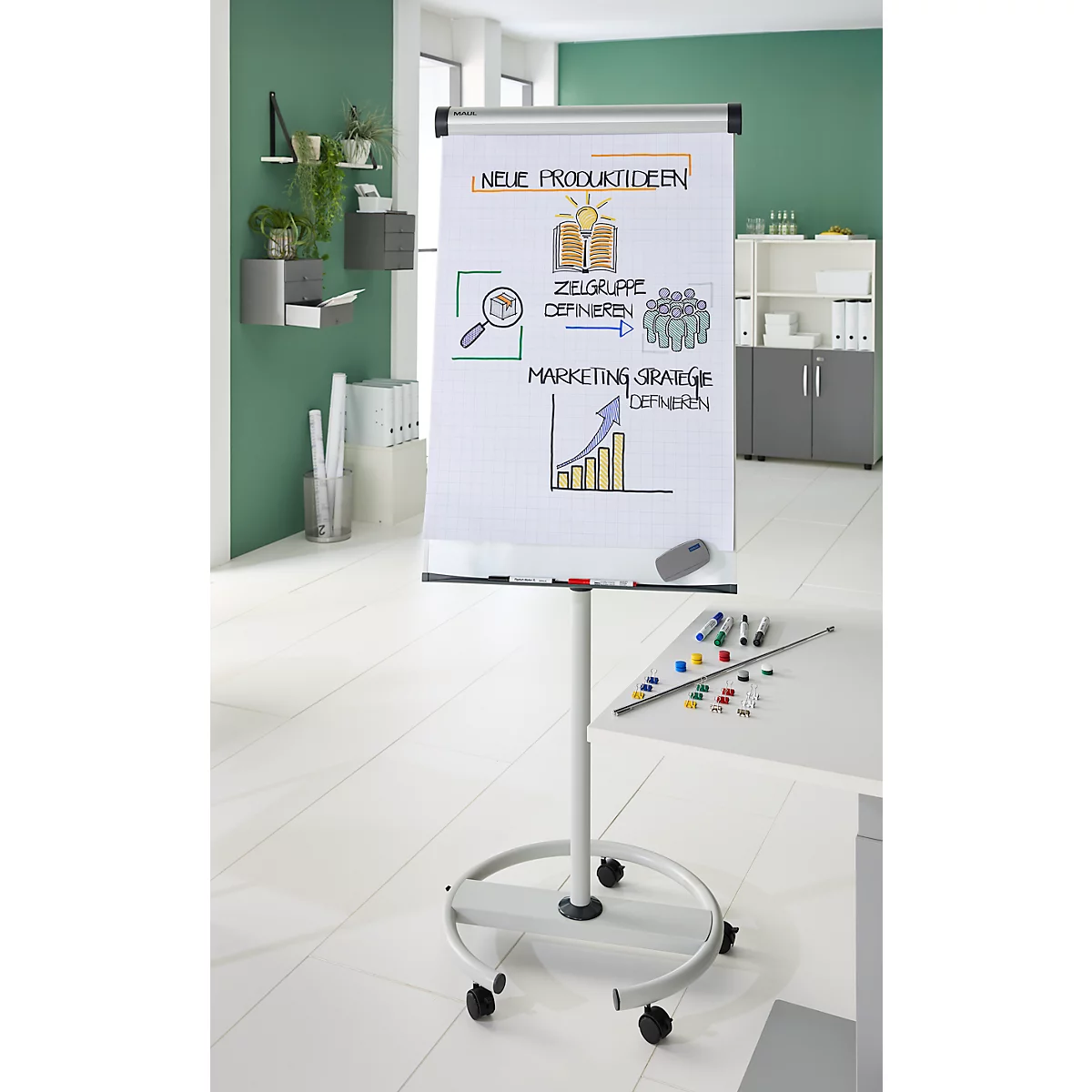 Flip-over met schetsen over productideeën; op kantoor. Planten en planken aan de muren.