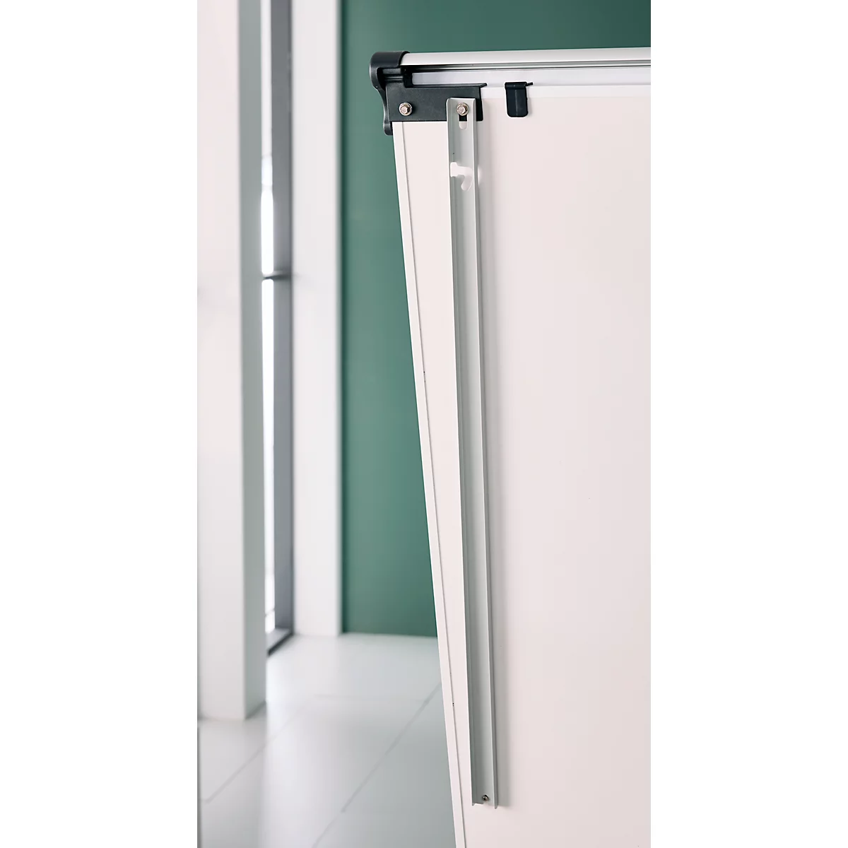 Close-up van een wit whiteboard, deels verborgen door een metalen frame, tegen een groene muur.