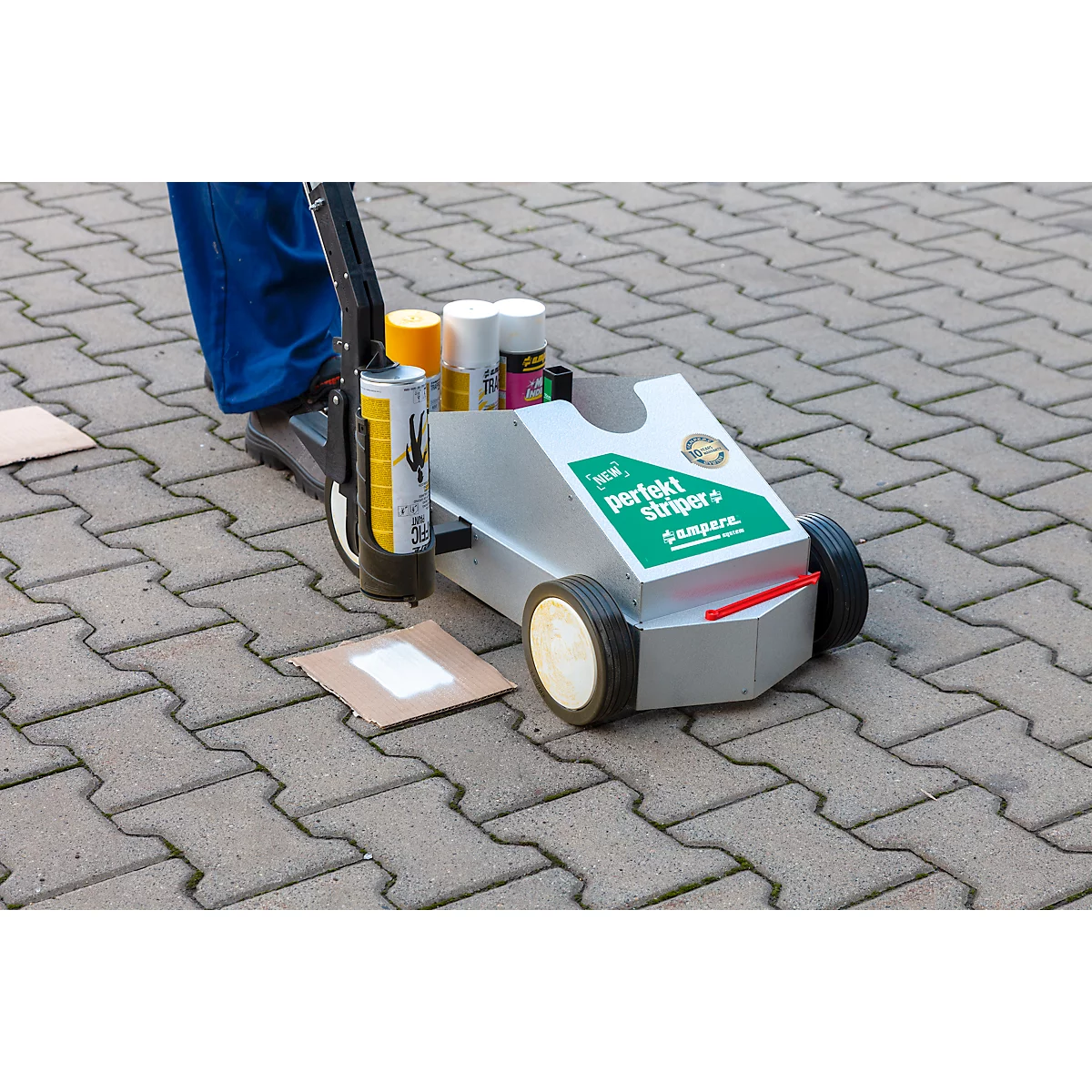 A person uses a wheeled cart to mark a line. The cart is loaded with paint and labeled 'perfect striper'.