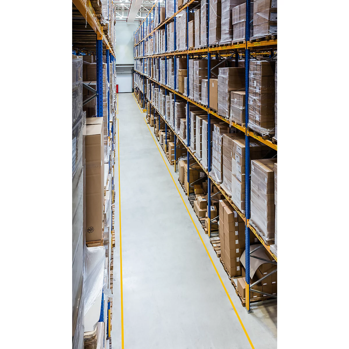 Warehouse interior with shelves stacked with packages and goods. Yellow line on the floor marks an aisle.