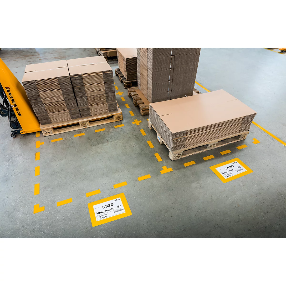 Pallets with cardboard boxes in a factory. Yellow markings on the floor and information signs.