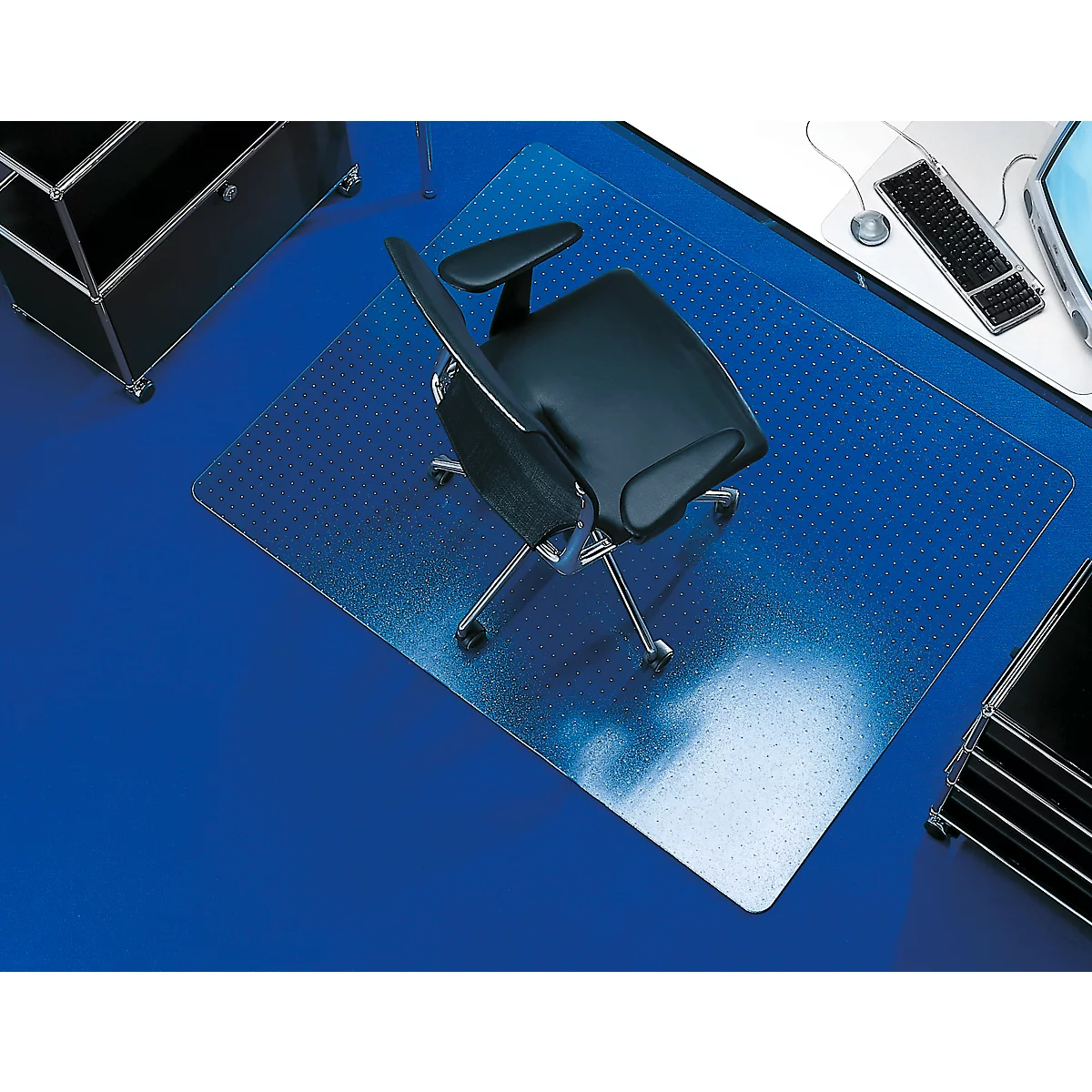 Office chair on a transparent floor protection mat. On a blue surface, a desk to the right.