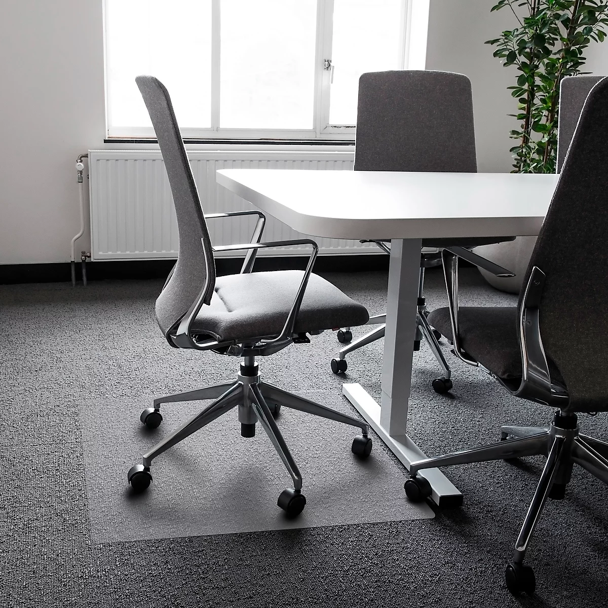 Bureaustoel met wielen voor een witte tafel. Grijs patroon tapijt, raam op de achtergrond.