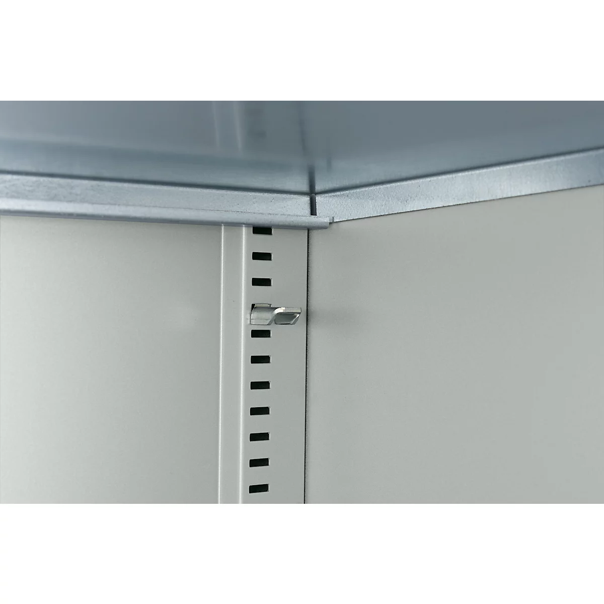 Innenansicht eines Metallschranks mit Beschlägen und Lochungen. Ein silberner Riegel hält die Schranktür geschlossen.