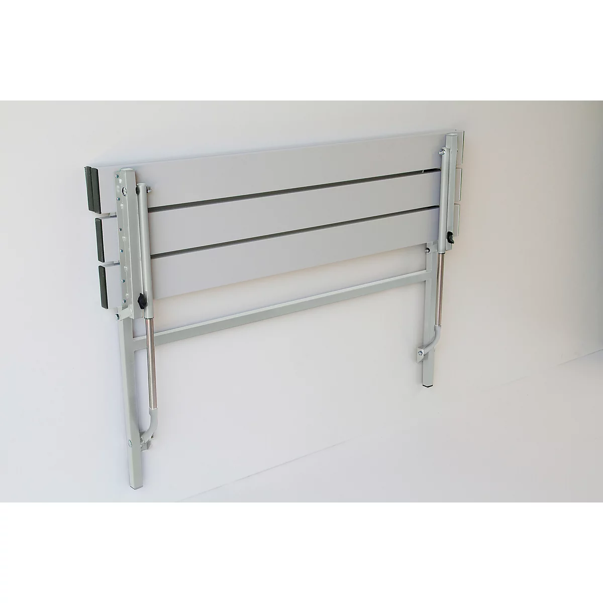 A gray, folded wall-mounted table with silver legs against a white wall.