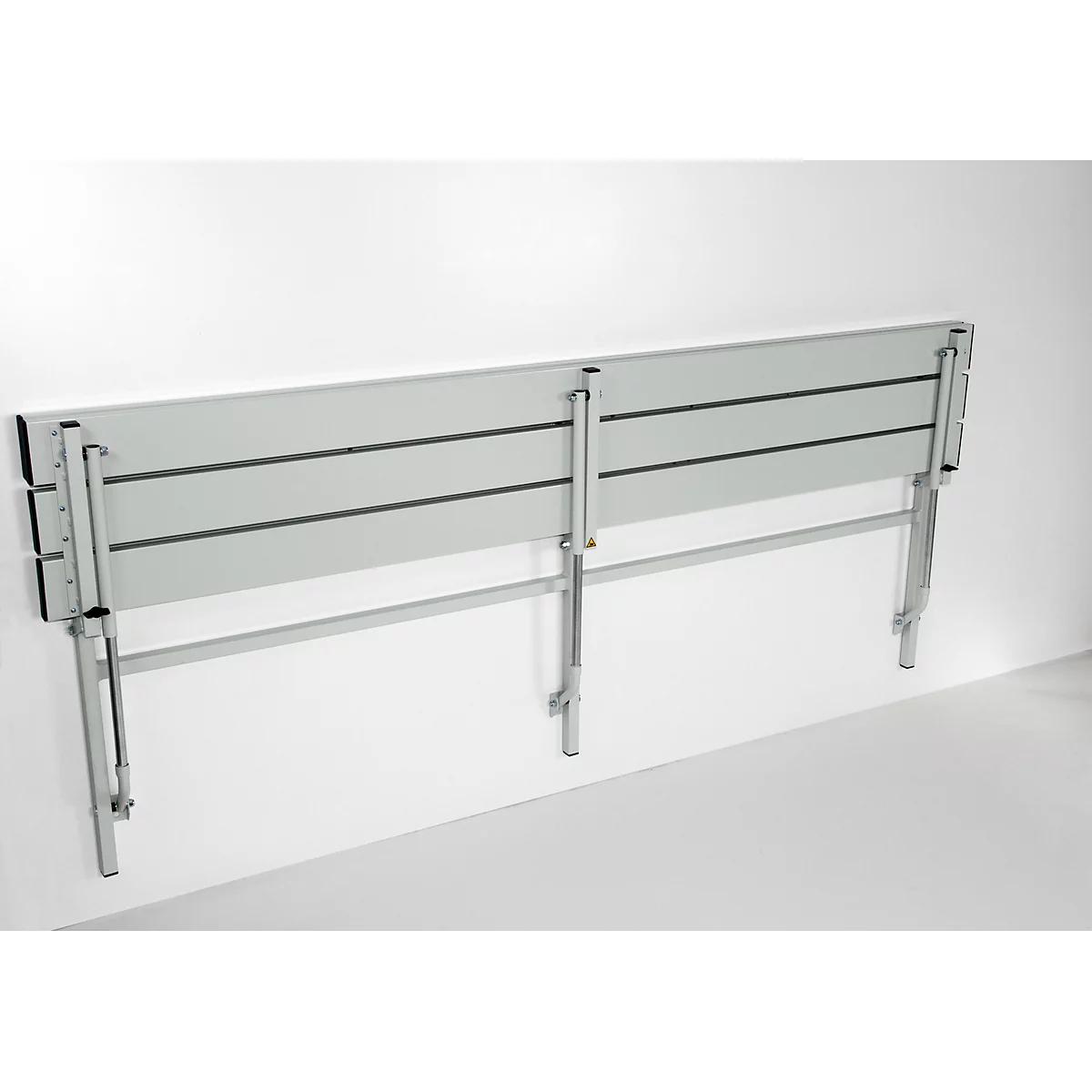 Grey, wall-mounted folding seat, made of metal. Three horizontal seat surfaces, attached to gray wall.