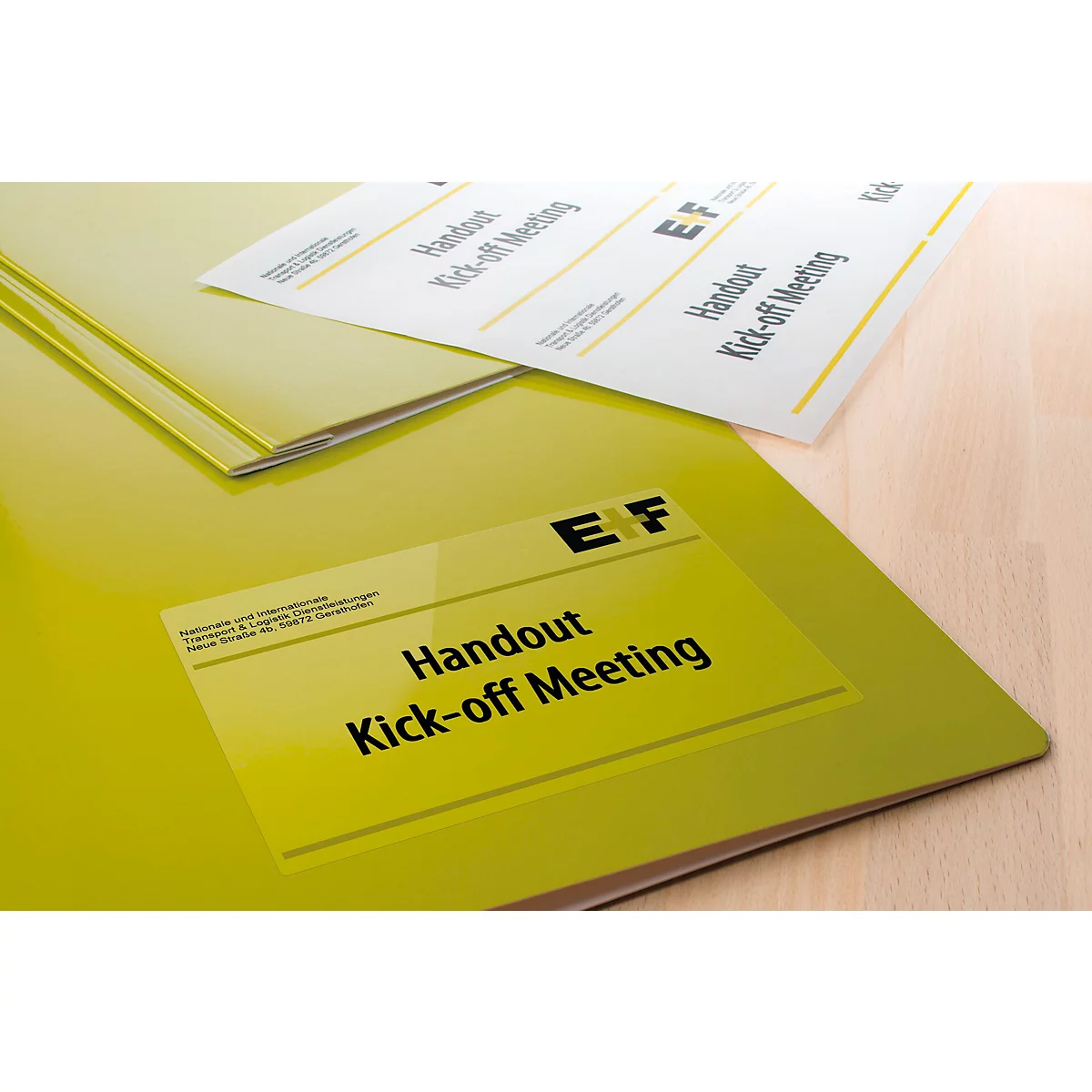 Gele mappen en vellen met de tekst "Handout Kick-off Meeting". De materialen liggen op een houten oppervlak.