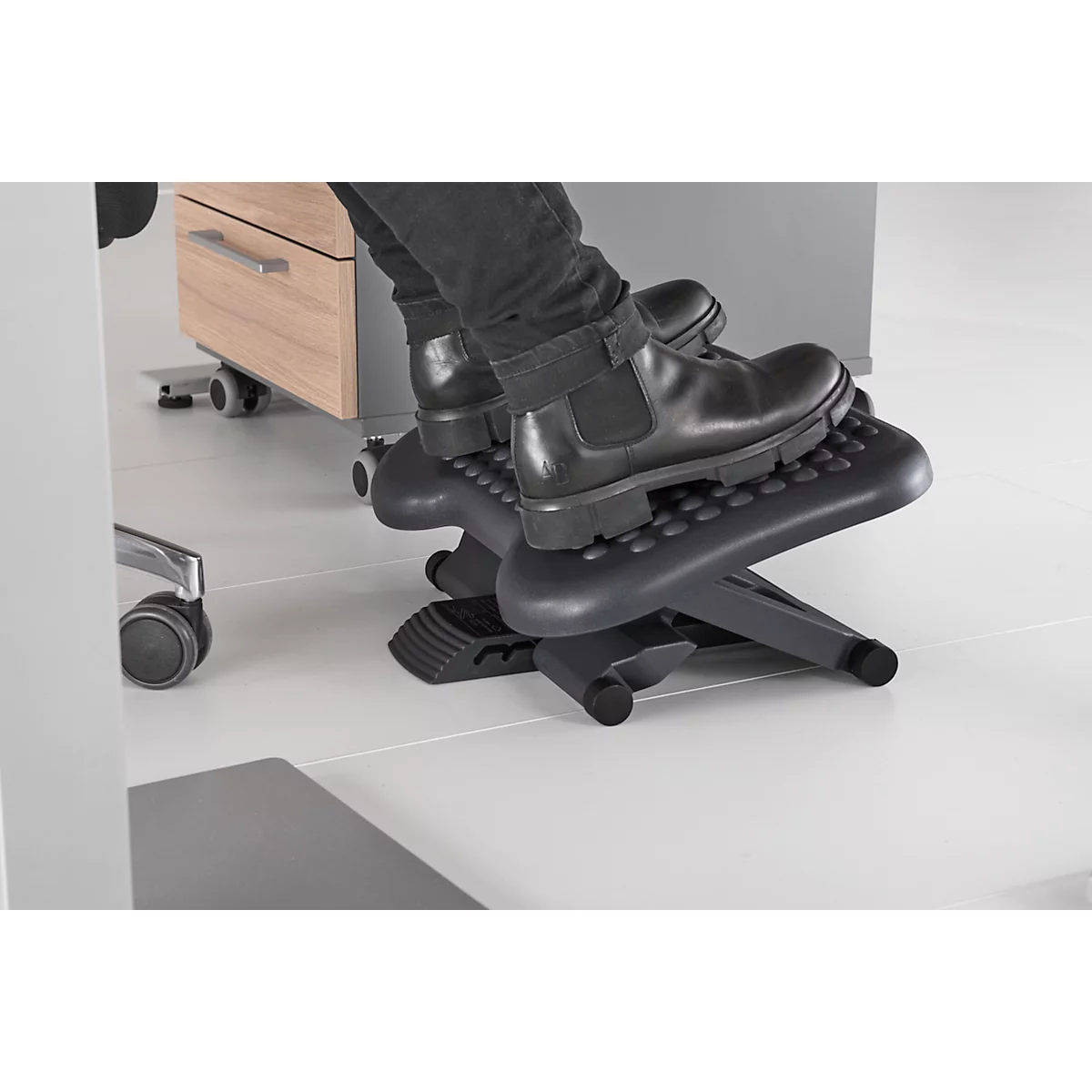 Feet on a black footrest, person wearing black pants and shoes, in the office.