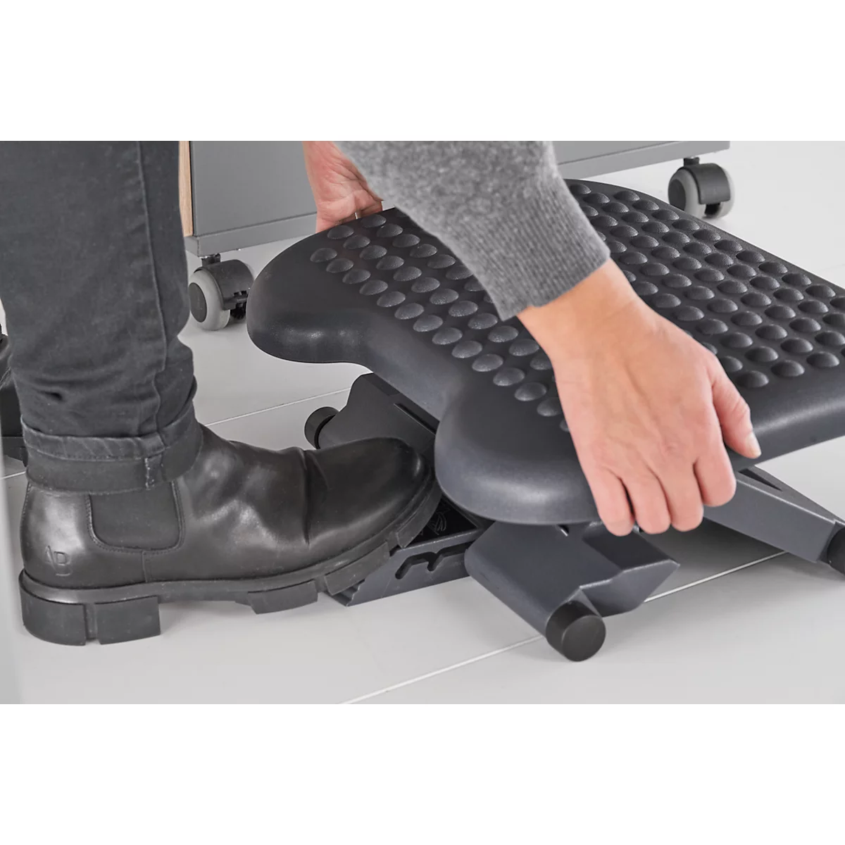 Person holding a black footrest, leg with shoe next to it.