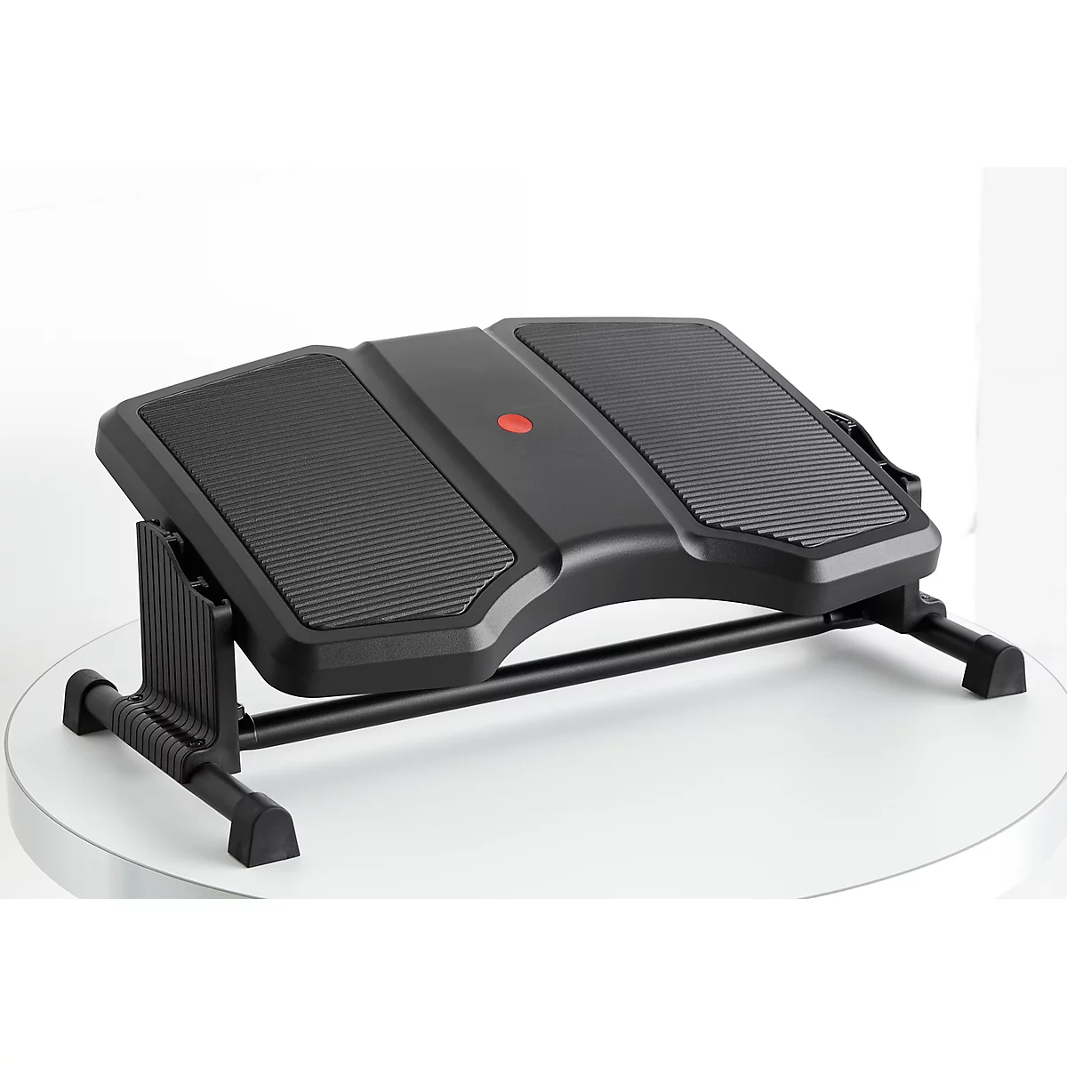 Black footrest with textured surface. On a white table. A red button in the middle.